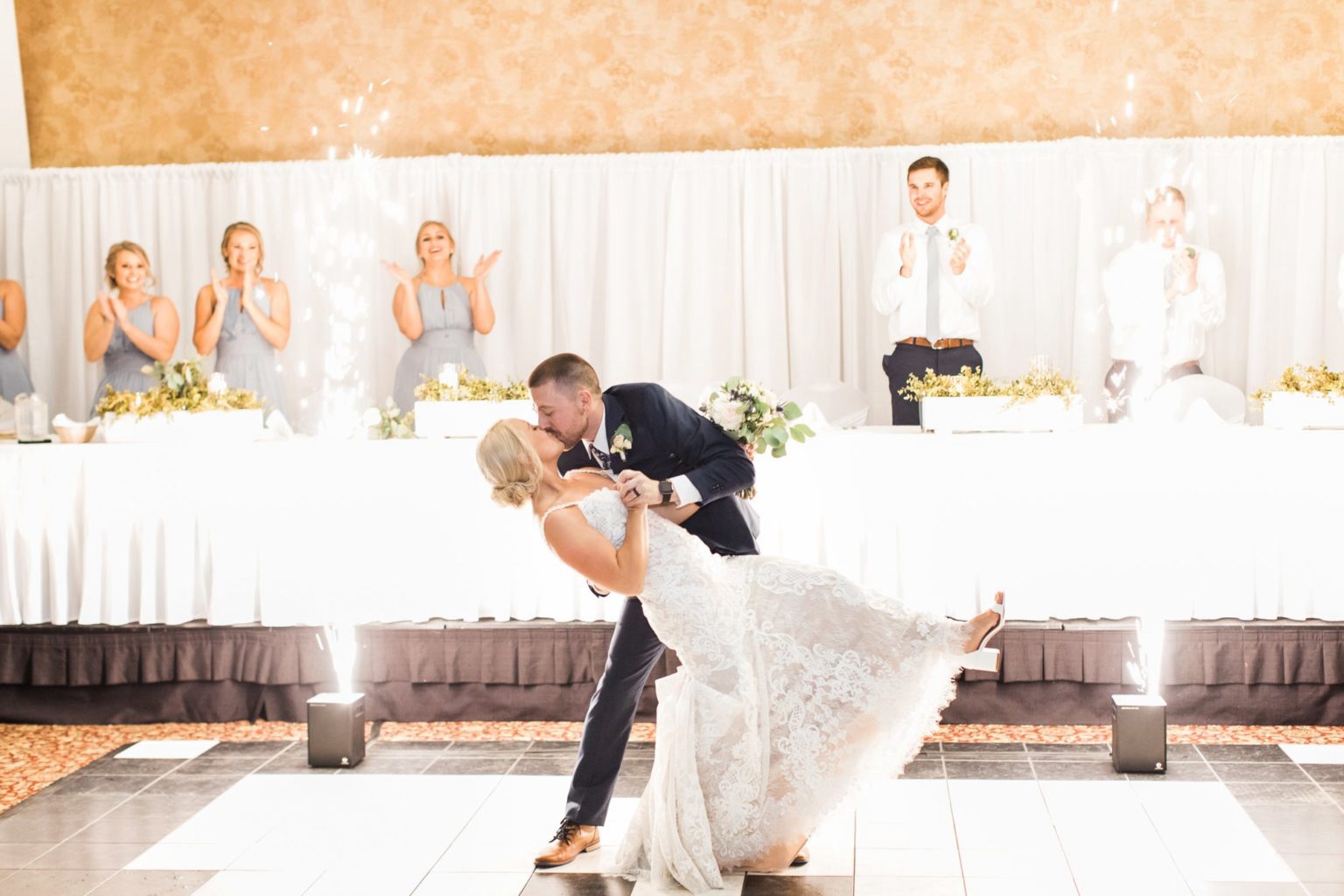 A couple dipping and kissing between two spark fountains at their wedding reception
